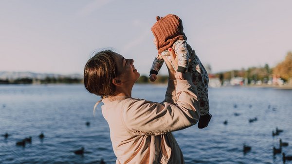 Matka držící své dítě ve vzduchu před jezerem