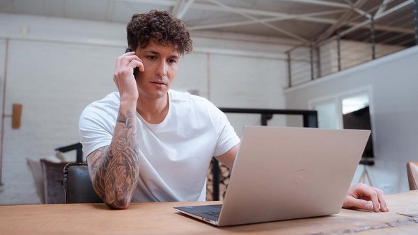 Junger Mann sitzt telefonierend vor einem Laptop.