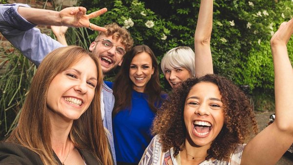 Pět přátel stojících blízko sebe a smějících se do kamery 