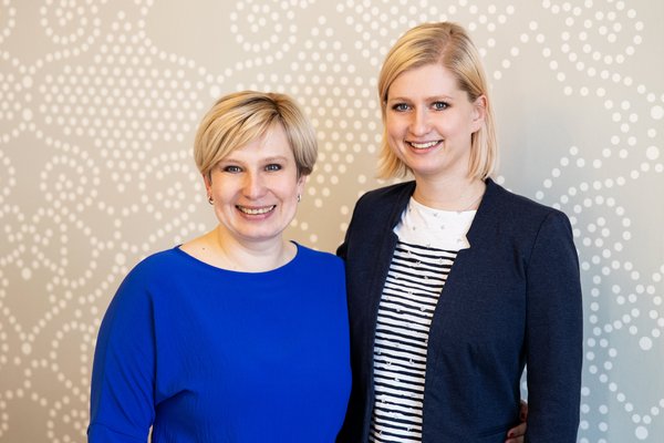 Dvě ženy stojící spolu v interiéru a usmívající se.