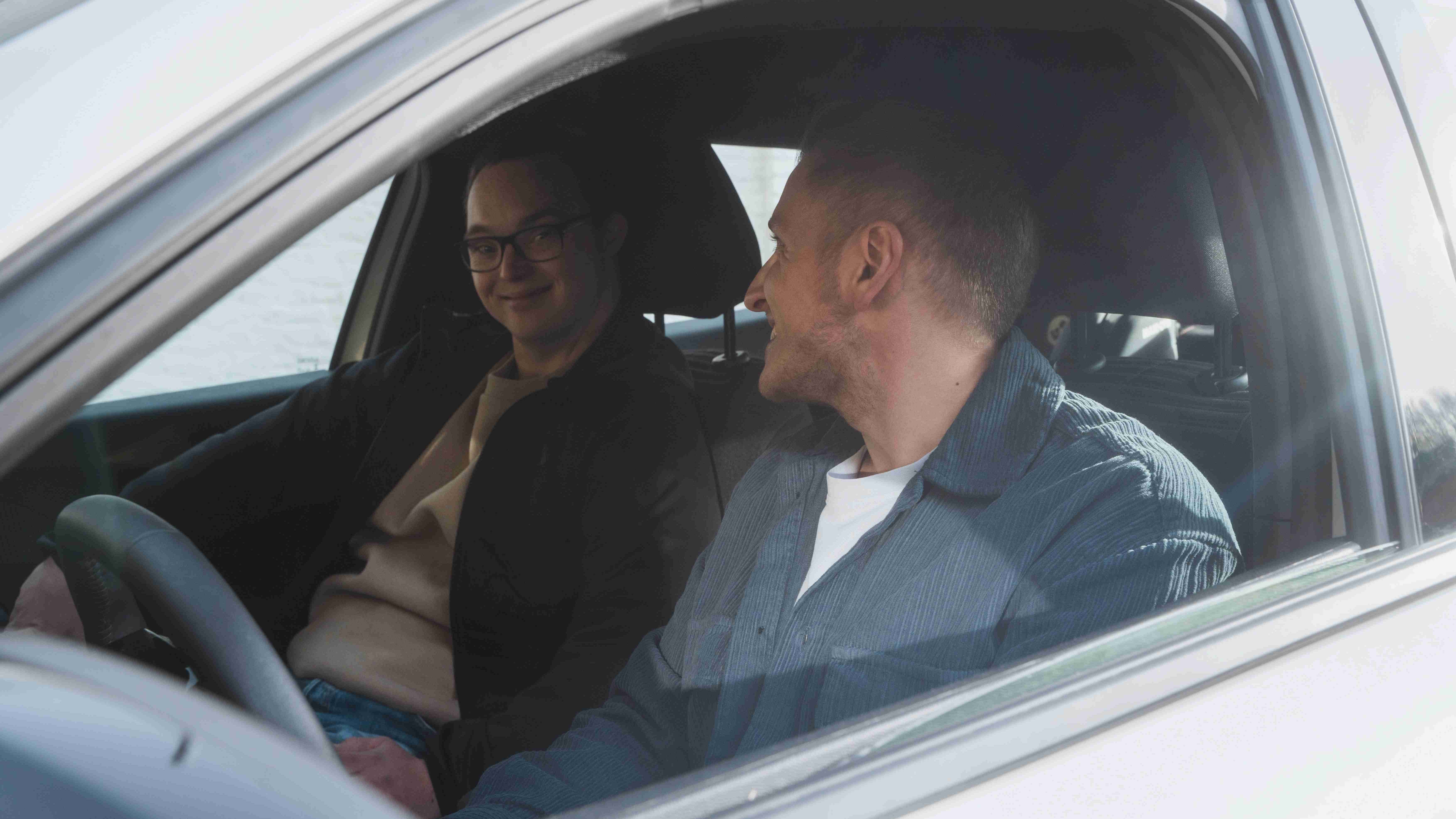 Dva mladí muži sedí v autě a usmívají se na sebe