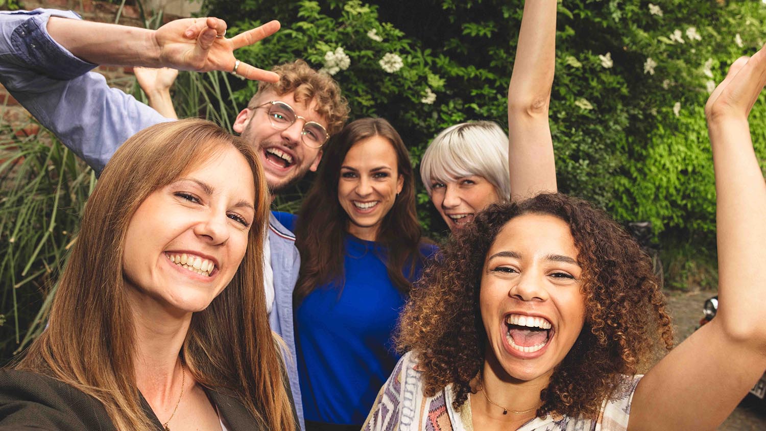 Plánování dovolené s přáteli – na co je potřeba se připravit Pět přátel stojících blízko sebe a smějících se do kamery