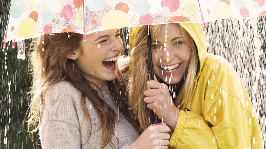 Dvě mladé ženy smějící se pod deštníkem