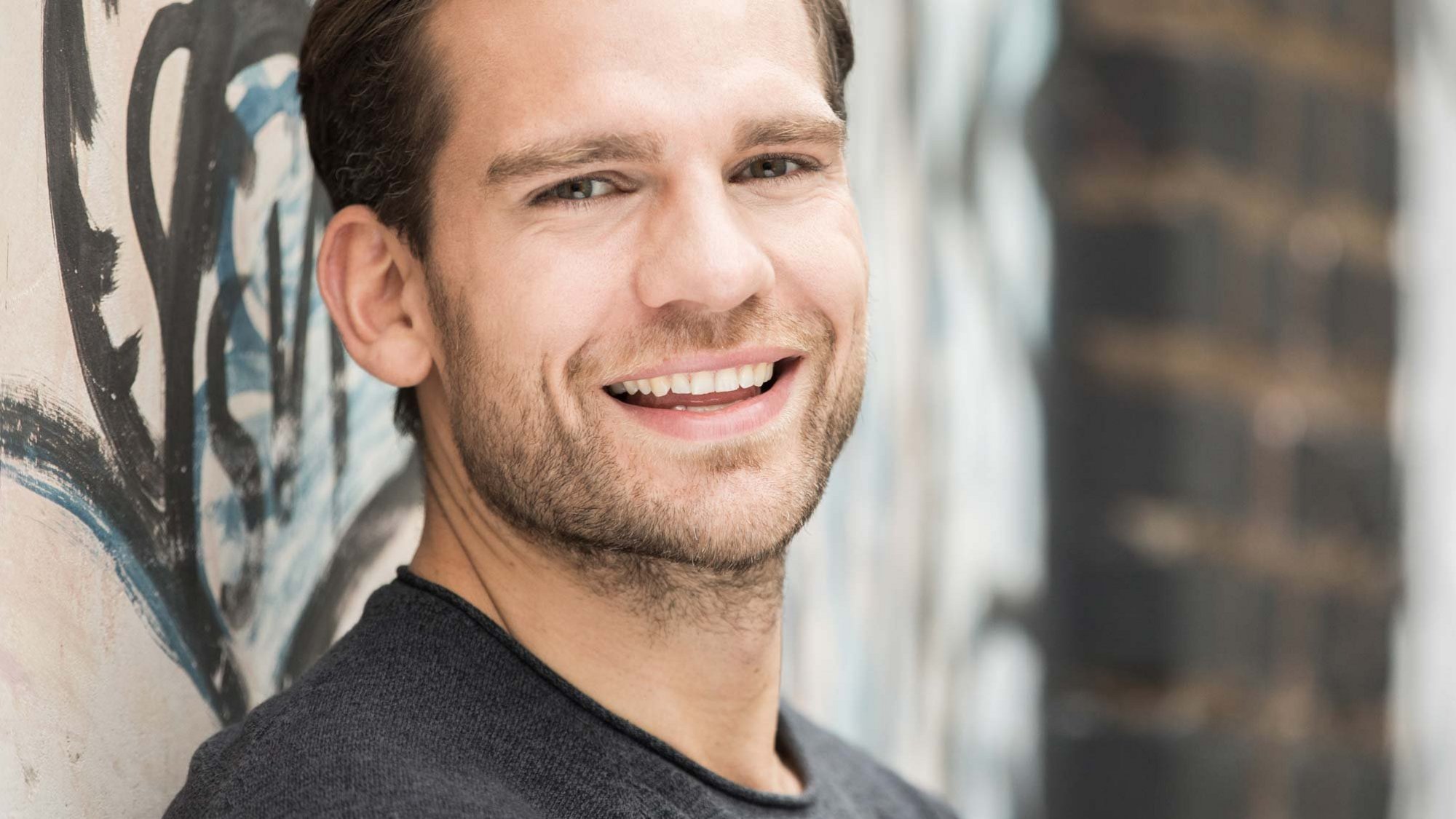Muž se usmívá a stojí u zdi.