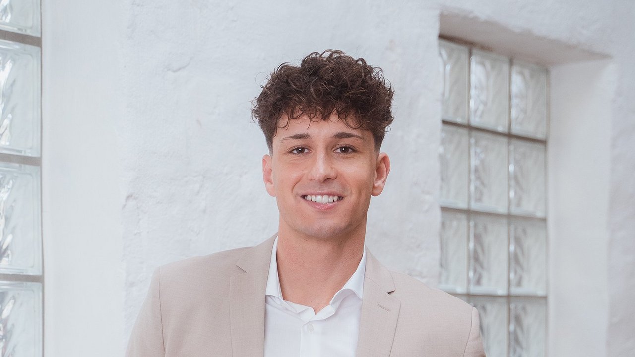 Muž stojí u zdi a usmívá se.